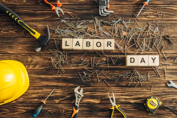 Top view of metal nails, safety helmet and instruments near cubes with labor day lettering on wooden surface — Stock Photo