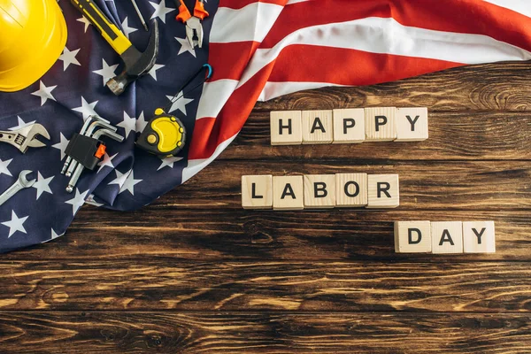 Draufsicht auf Schutzhelm und Instrumente in der Nähe von Happy Labor Day Schriftzug in der Nähe der amerikanischen Flagge auf Holzoberfläche — Stockfoto