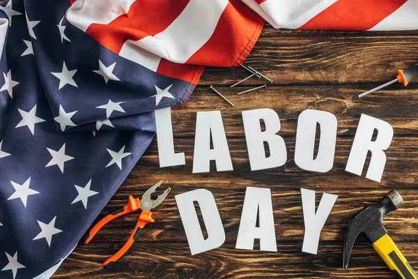 Top view of flag of america with stars and stripes near labor day lettering and instruments on wooden surface — Stock Photo