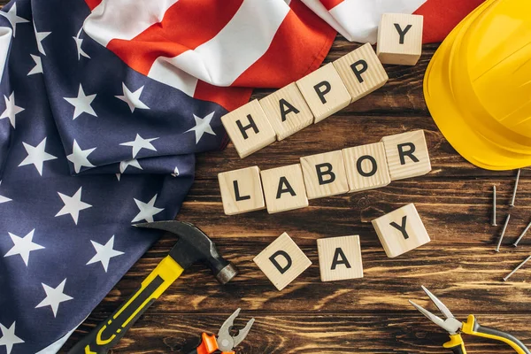 Draufsicht auf amerikanische Flagge und Instrumente in der Nähe von Schutzhelm und Happy Labor Day Schriftzug auf Holzoberfläche — Stockfoto