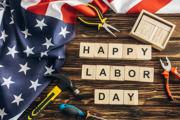 Draufsicht auf amerikanische Flagge und Instrumente in der Nähe von Happy Labor Day Schriftzug auf Holzoberfläche — Stockfoto