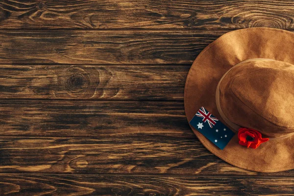 Vista superior do chapéu de feltro, flor artificial e bandeira australiana na superfície de madeira, conceito de dia anzac — Fotografia de Stock