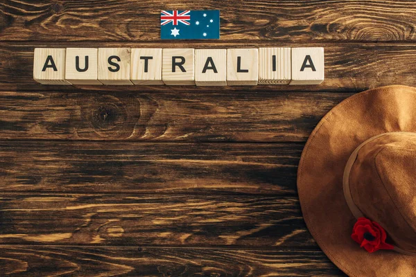 Vista superior da flor artificial, chapéu de feltro e bandeira australiana perto de cubos com letras austrália na superfície de madeira, conceito de dia anzac — Fotografia de Stock