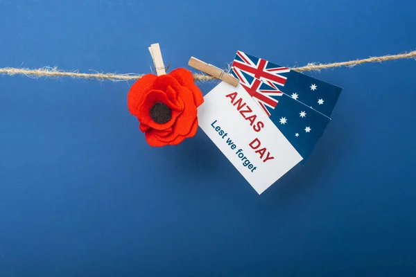 Rope, clothespins and card with anzas day lettering near artificial flower and flags of australia on blue — Stock Photo