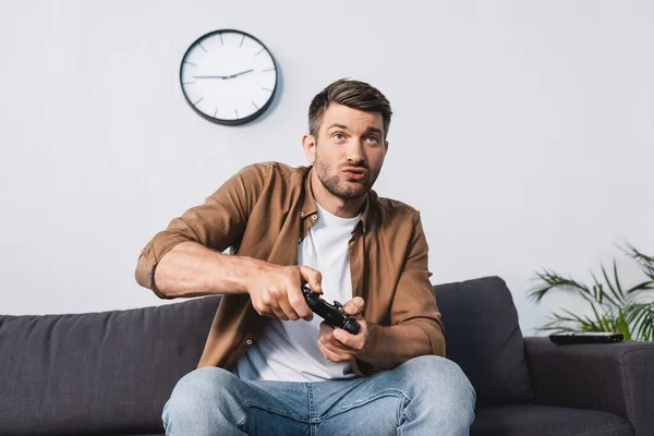 KYIV, UKRAINE - JUNE 9, 2020: excited man playing video game with joystick while sitting on sofa — Stock Photo