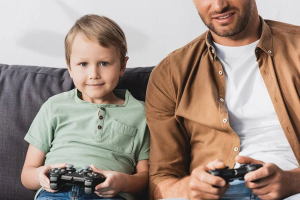 KIEW, UKRAINE - 9. JUNI 2020: Ausgeschnittene Ansicht eines lächelnden Mannes in der Nähe eines glücklichen Sohnes beim Videospiel mit Joystick — Stockfoto