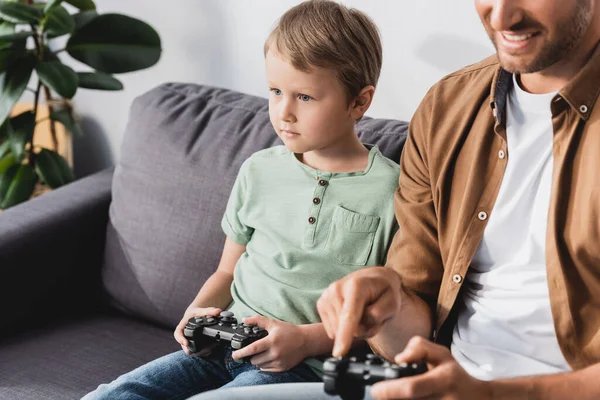 KYIV, UKRAINE - JUNE 9, 2020: cropped view of smiling man and attenive son playing video game wih joysticks — Stock Photo