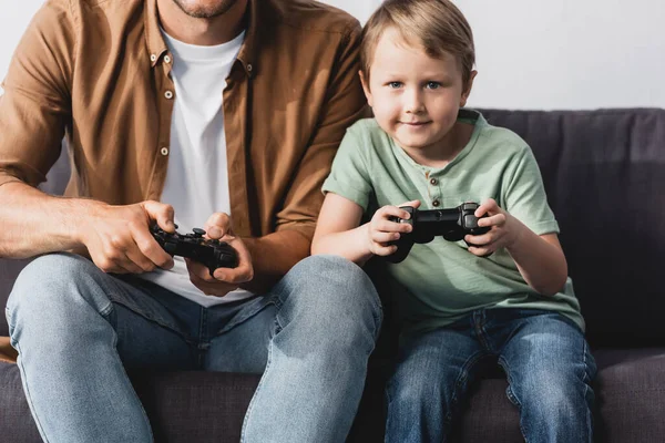 KYIV, UKRAINE - JUNE 9, 2020: cropped view of man with attentive son playing video game with joysticks — Stock Photo