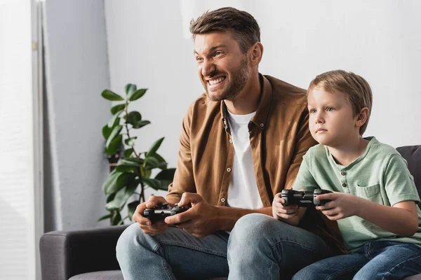 KYIV, UKRAINE - JUNE 9, 2020: excited father and concentrated son playing video game with joysticks — Stock Photo
