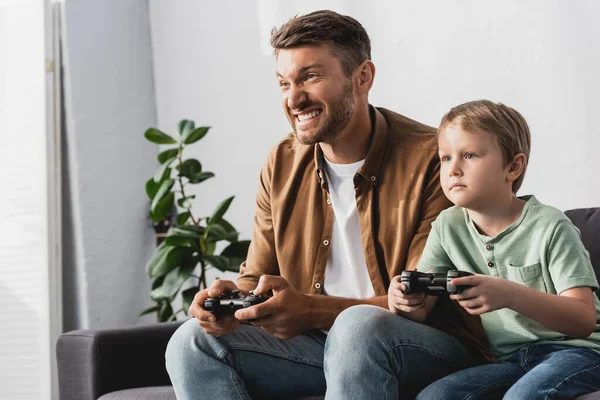 KYIV, UKRAINE - 9 JUIN 2020 : père excité et fils concentré jouant à un jeu vidéo avec des joysticks — Photo de stock