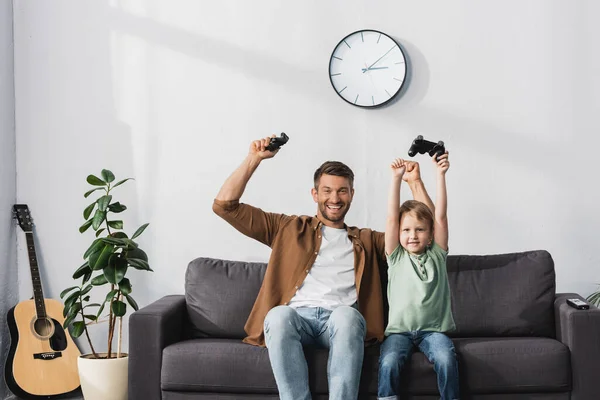 KYIV, UKRAINE - JUNE 9, 2020: happy father and son holding joysticks and showing winner gestures — Stock Photo