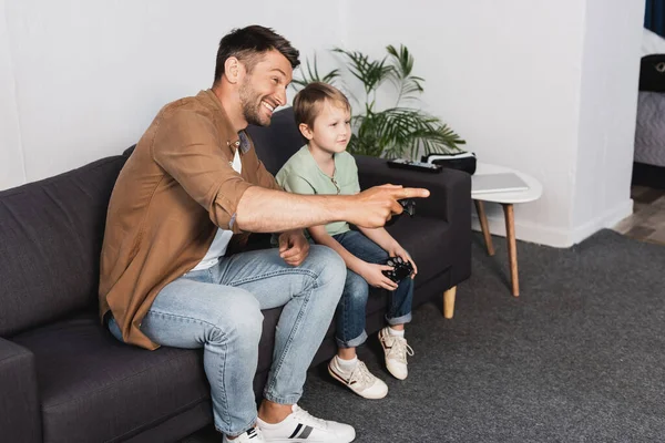 KIEW, UKRAINE - 9. JUNI 2020: Fröhlicher Vater zeigt mit dem Finger in die Nähe seines konzentrierten Sohnes, der den Steuerknüppel hält — Stockfoto