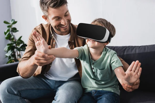 Homme souriant touchant les mains du fils gai dans le casque vr — Photo de stock