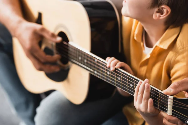 Vista recortada de padre enseñando hijo cómo tocar la guitarra acústica, enfoque selectivo - foto de stock