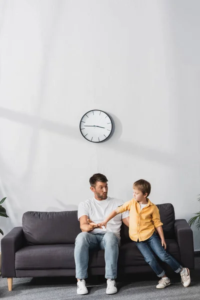 Батько і син тримають руки, сидячи на дивані вдома — стокове фото