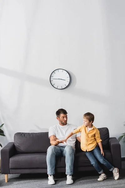Father and son holding hands while sitting on sofa at home — Stock Photo