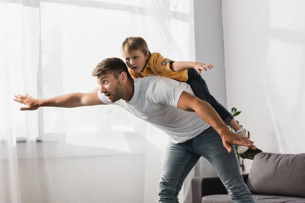 Handsome father piggybacking happy son imitating flying with outstretched hands — Stock Photo