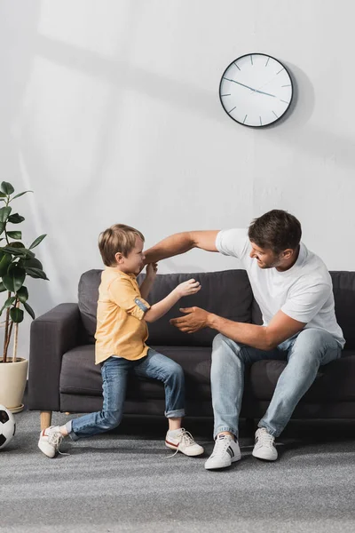 Feliz pai e filho se divertindo enquanto brincando lutando no sofá em casa — Fotografia de Stock