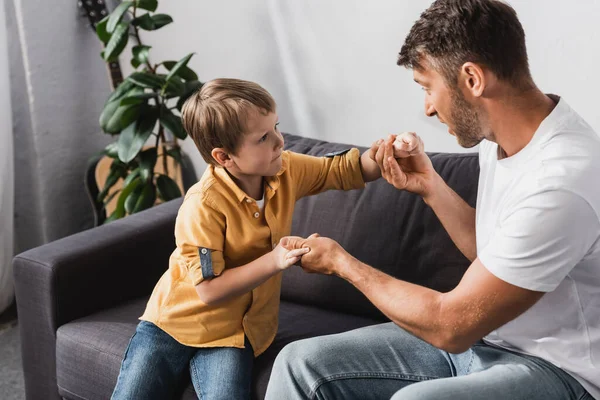 Father and son holding hands and looking at each other while sitting on sofa at home — Stock Photo