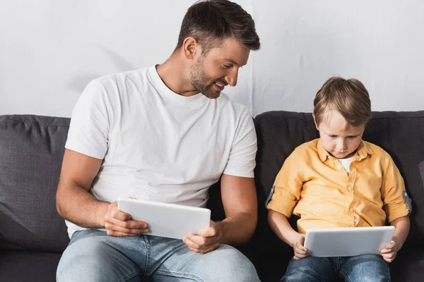 Lächelnder Vater blickt auf digitales Tablet in den Händen des aufmerksamen Sohnes — Stockfoto