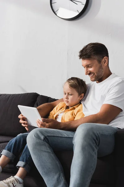 Homem feliz com filho adorável usando tablet digital juntos enquanto sentado no sofá — Fotografia de Stock