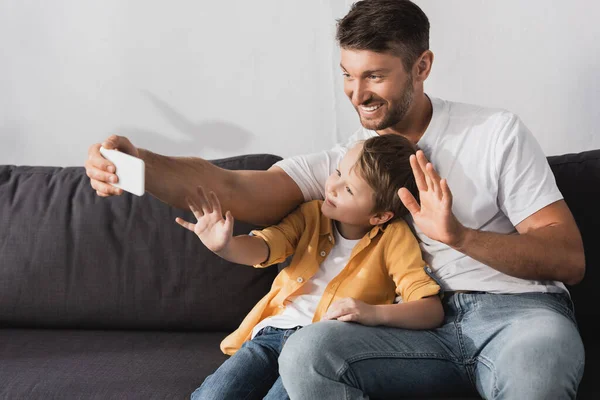 Alegre pai e filho acenando mãos dring vídeo chat no smartphone — Fotografia de Stock