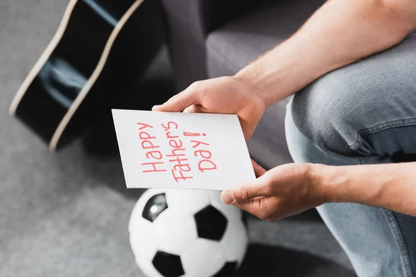 Recortado vista de hombre sosteniendo feliz padre día tarjeta cerca de pelota de fútbol - foto de stock