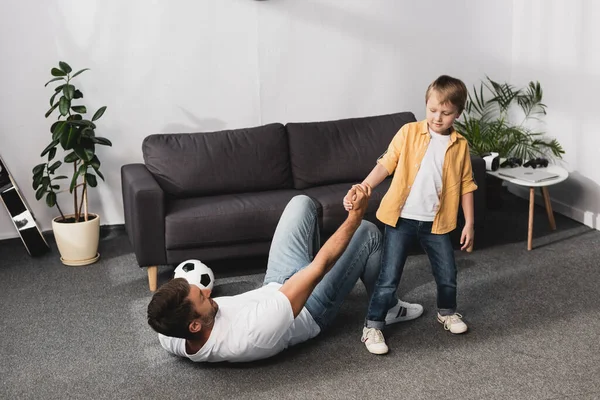 Netter Junge reicht gefallenem Vater mit Fußballball die Hand — Stockfoto