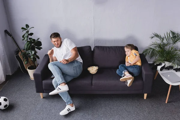 Frightened, worried father and som watching tv on sofa at home — Stock Photo