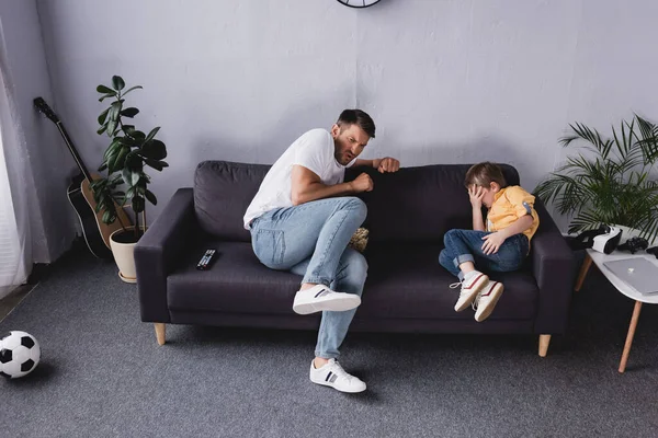 Испуганные, обеспокоенные отец и сын смотрят телевизор на диване дома — стоковое фото