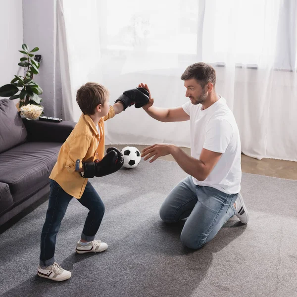 Guapo hombre luchando con lindo hijo en guantes de boxeo en el suelo - foto de stock