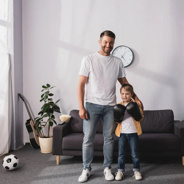 Lächelnder Vater steht neben Sohn in Boxhandschuhen und berührt seine Schulter — Stockfoto