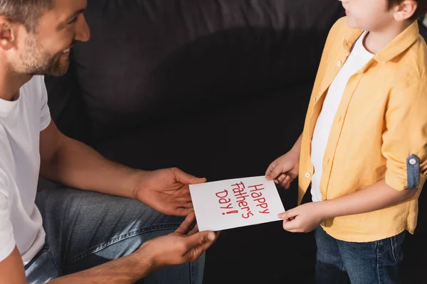 Cropped view of man taking happy fathers day card from adorable son — Stock Photo