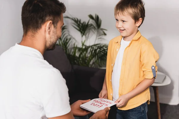 Feliz niño regalando feliz día de los padres tarjeta a padre - foto de stock