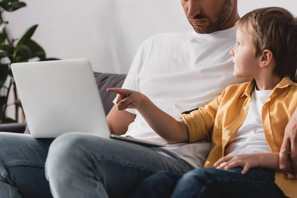 Cropped view of man with laptop sitting near son pointing with finger at screen — Stock Photo