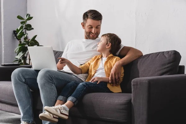 Sorrindo pai olhando para filho adorável apontando com o dedo para laptop — Fotografia de Stock