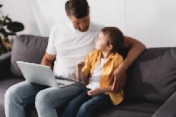 Foyer sélectif du père et du fils assis sur le canapé, parler et utiliser un ordinateur portable — Photo de stock