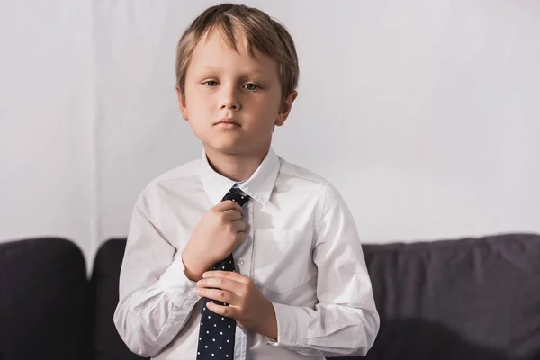 Serious boy in white shirt putting tie on and looking at camera — Stock Photo
