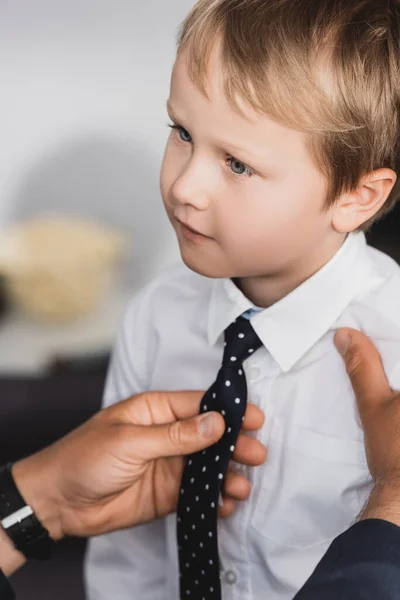 Cropped view of businessman putting tie on adorable, serious son at home — Stock Photo