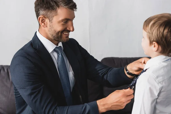 Счастливый бизнесмен надевает галстук на очаровательного сына дома — стоковое фото