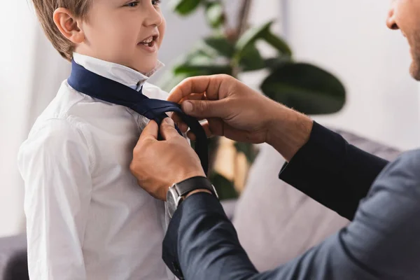 Обрізаний вид бізнесмена кладе краватку на щасливого, чарівного сина вдома — стокове фото