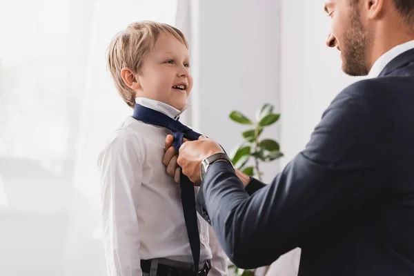 Businessman in formal wear putting tie on happy son at home — Stock Photo