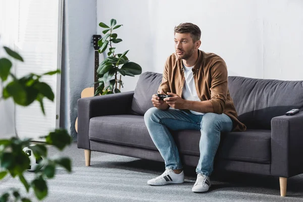 KYIV, UKRAINE - JUNE 9, 2020: selective focus of attentive man sitting on sofa and playing video game — Stock Photo