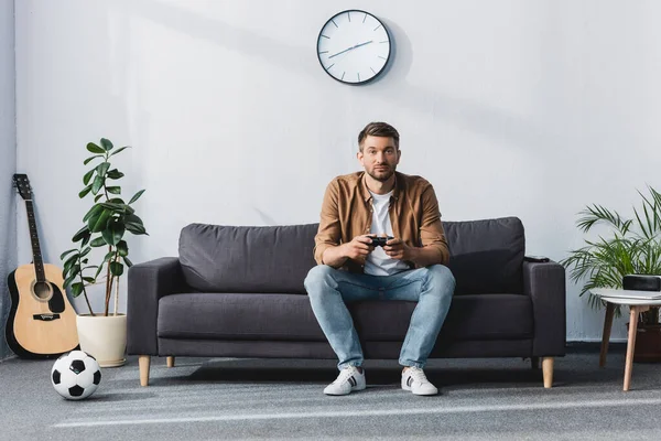 KYIV, UKRAINE - JUNE 9, 2020: handsome man playing video game near acoustic guitar, soccer ball and plants — Stock Photo