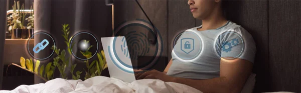 Panoramic crop of mixed race freelancer using laptop near virtual icons in bedroom — Stock Photo