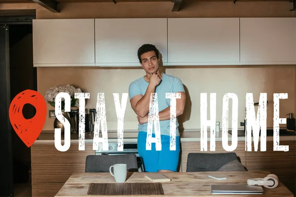 Nachdenklicher Mischlingsmann steht neben Kaffeetasse, Buch, Kopfhörer, Laptop und bleibt zu Hause — Stockfoto