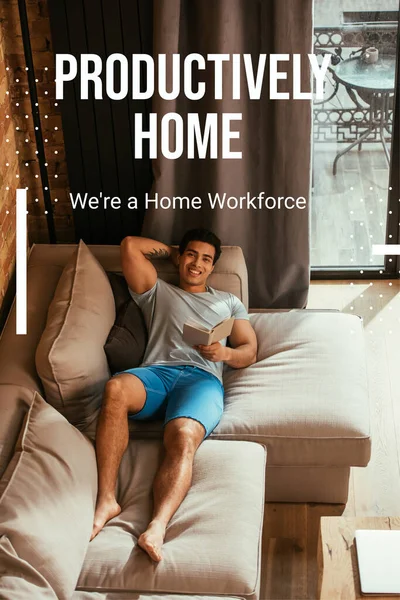 Happy mixed race man reading book while chilling on sofa near productively home, were a home workforce lettering — Stock Photo