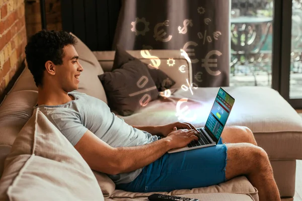 Happy mixed race man chilling and using laptop with SportsBet website on screen near  money signs illustration — Stock Photo