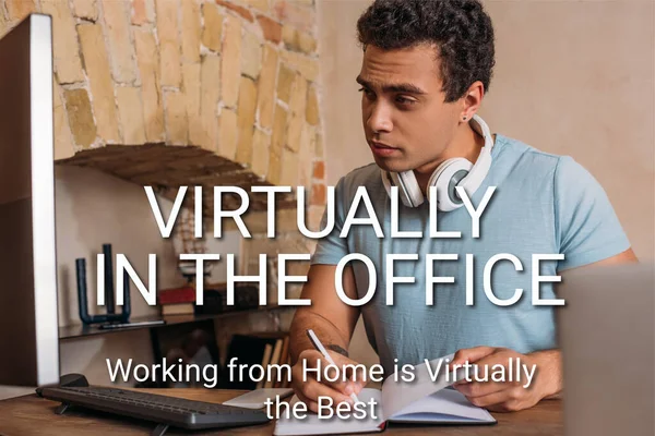 Selective focus of handsome mixed race freelancer writing in notebook near computer monitor and virtually in the office, working from home is virtually the best lettering — Stock Photo