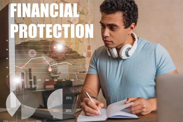 Selective focus of handsome mixed race freelancer writing in notebook near computer monitor and financial protection lettering — Stock Photo